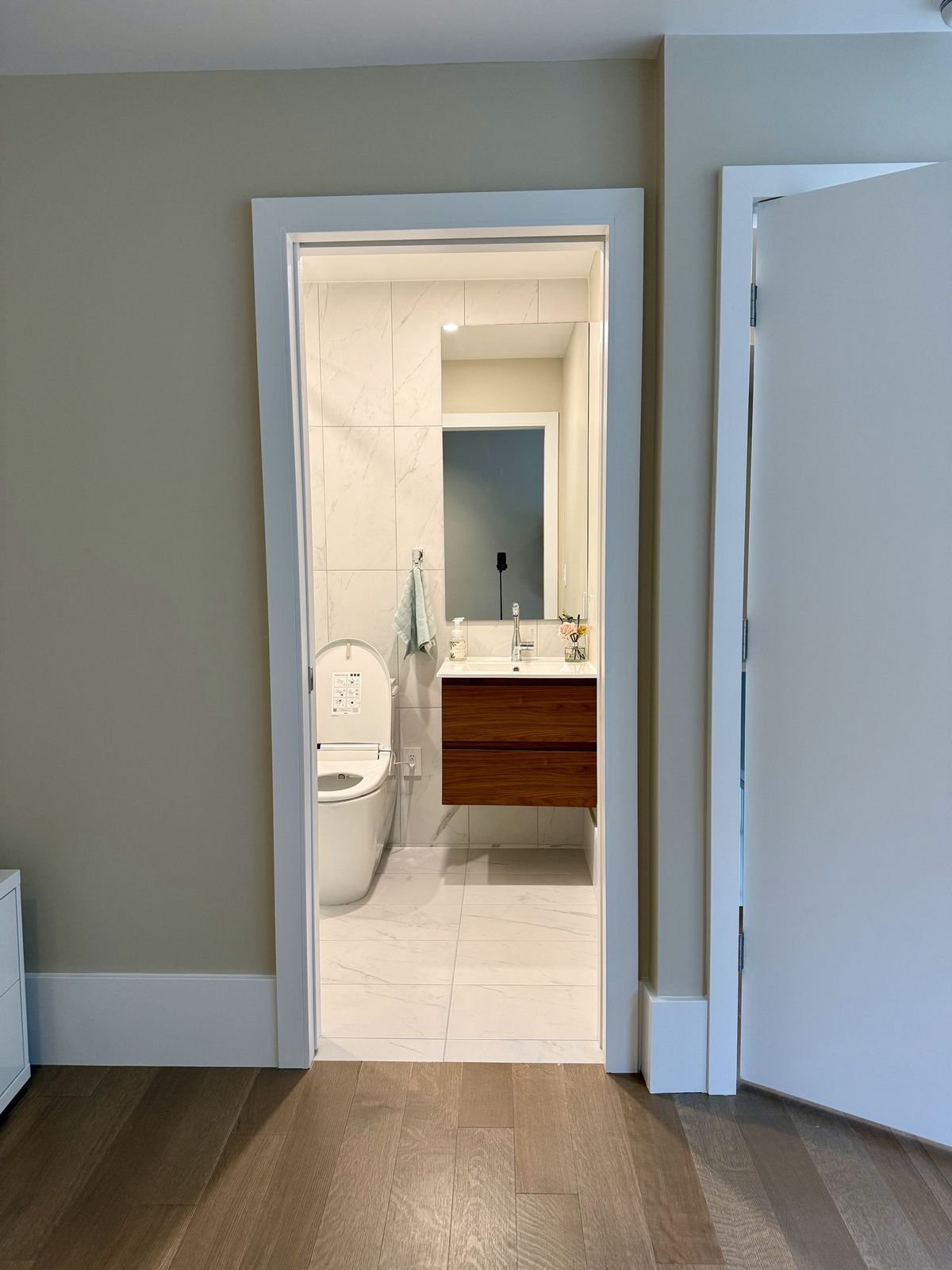 View through the doorway into a new ensuite with marble-look tile and a walnut floating vanity in West Vancouver