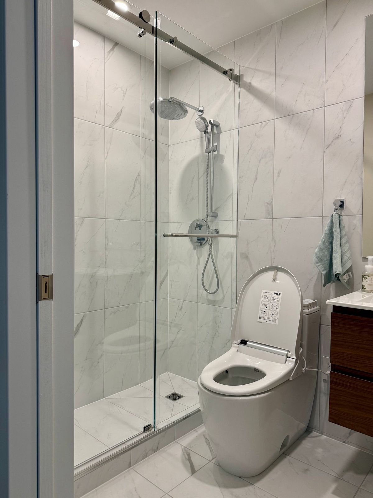 New West Vancouver ensuite with a sliding glass shower, marble-look porcelain tile and walnut vanity