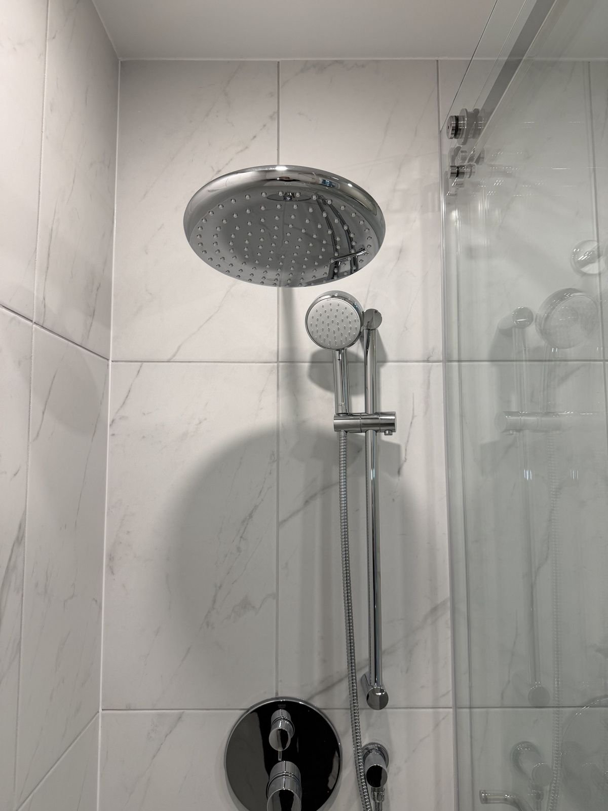 Grohe rain shower head and hand shower on a slide bar with marble-look tile in a West Vancouver bathroom addition
