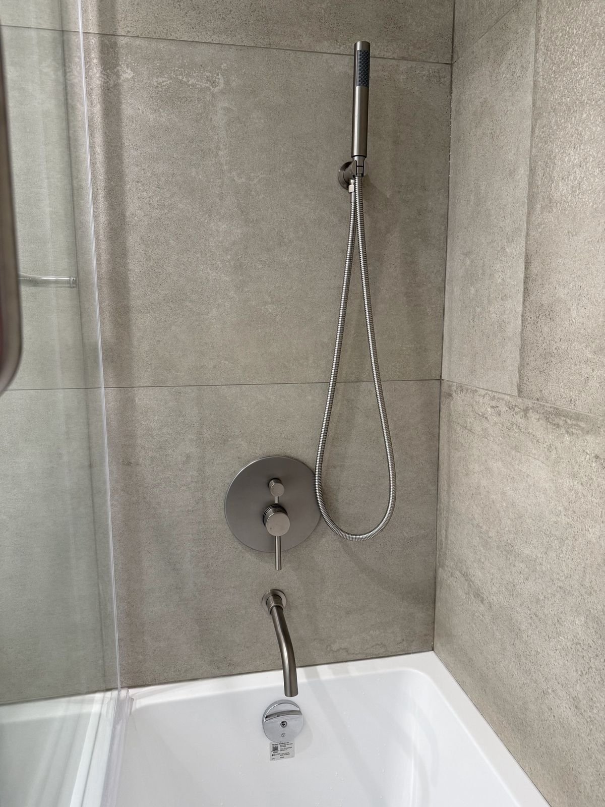 Brushed nickel hand shower, pressure-balance valve and tub spout on large-format porcelain tile in a Yaletown condo