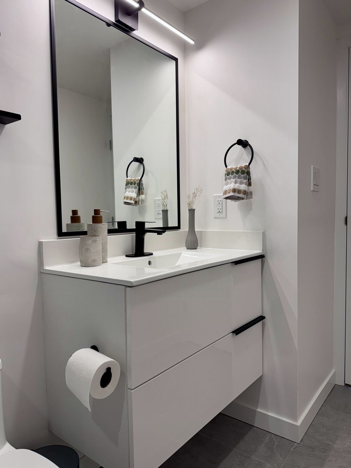 After: white floating vanity with a black faucet and black-framed mirror in a renovated Yaletown condo bathroom