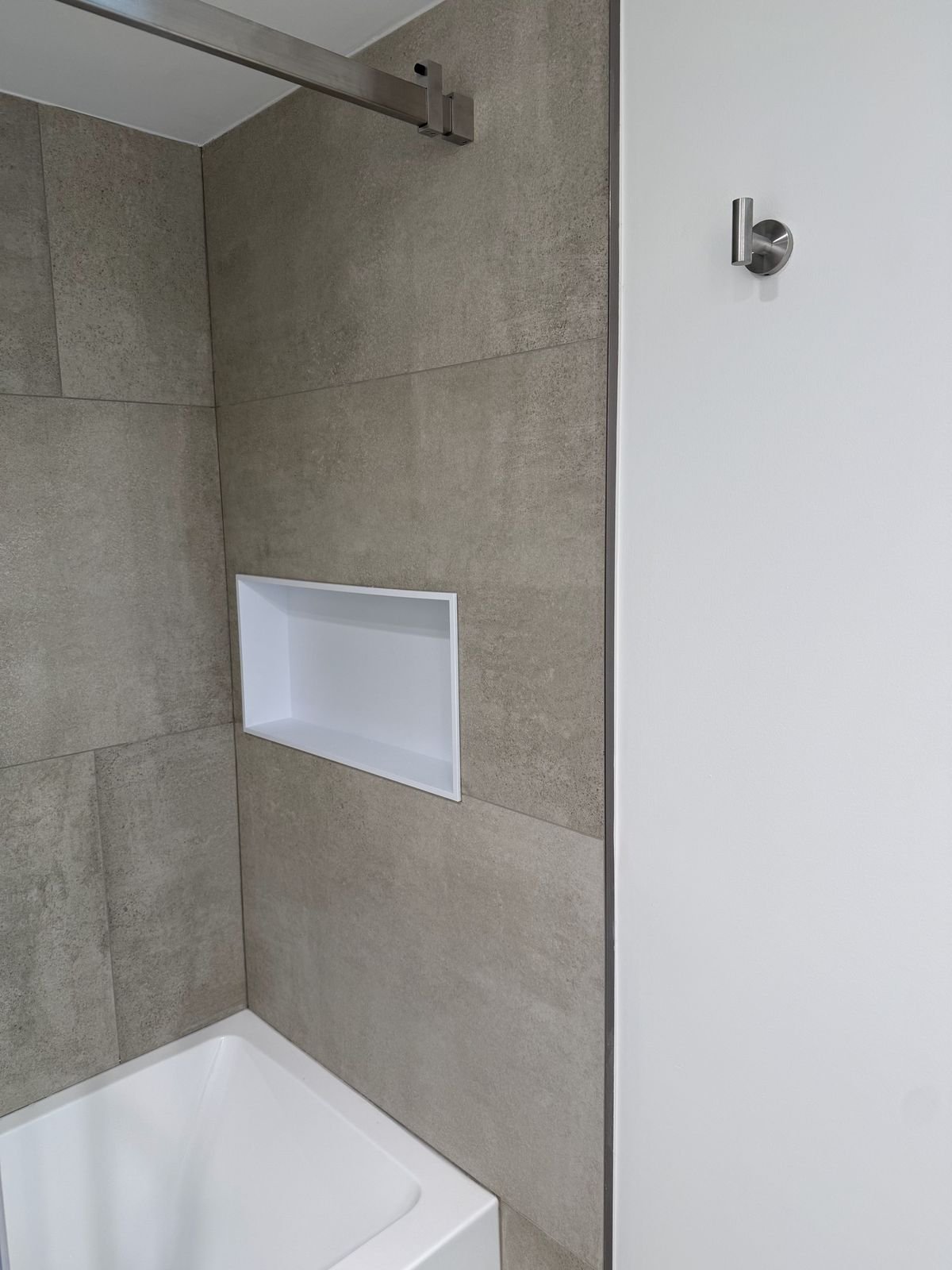 Horizontal recessed shower niche in concrete-look porcelain tile above a new bathtub in a Yaletown condo