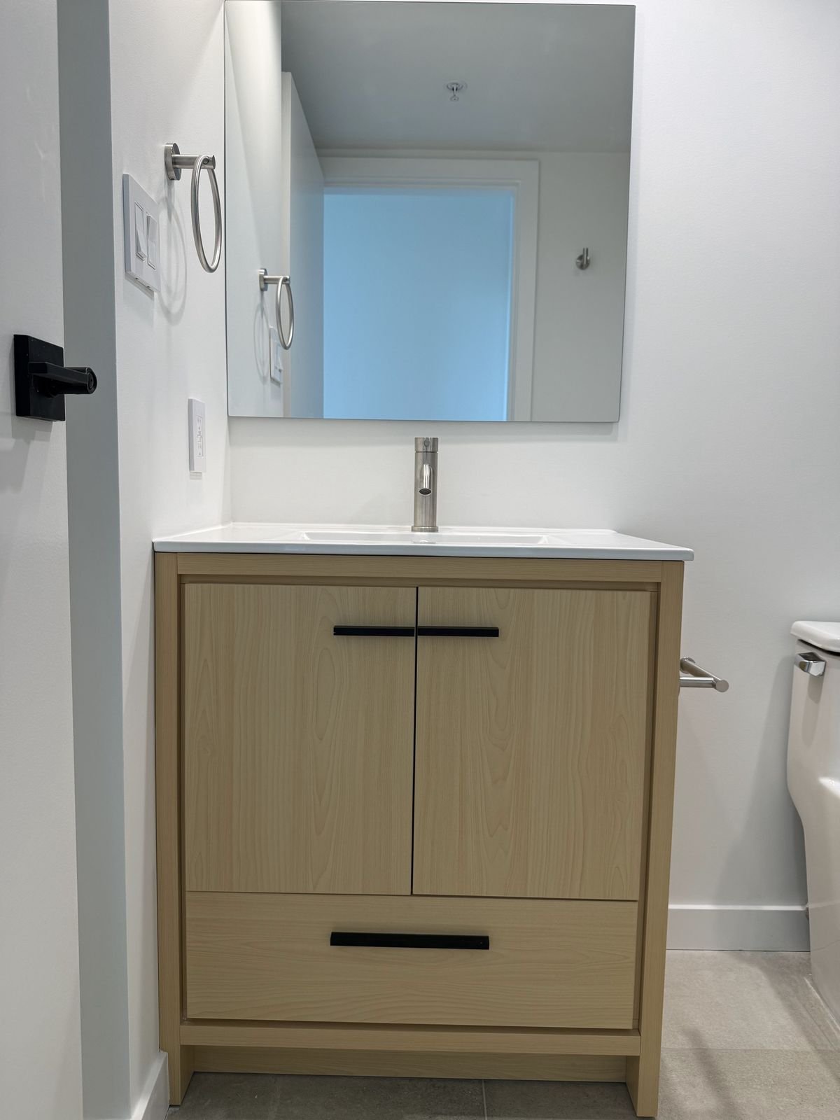 Light oak 30-inch vanity with matte black pulls and a frameless mirror in a renovated Yaletown condo bathroom