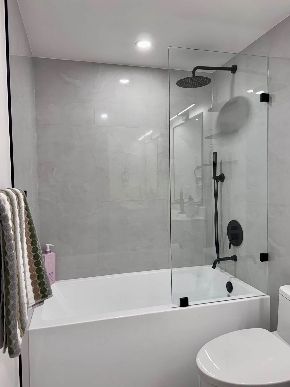 Matte black rain shower and hand shower behind a frameless glass tub screen in a Yaletown condo