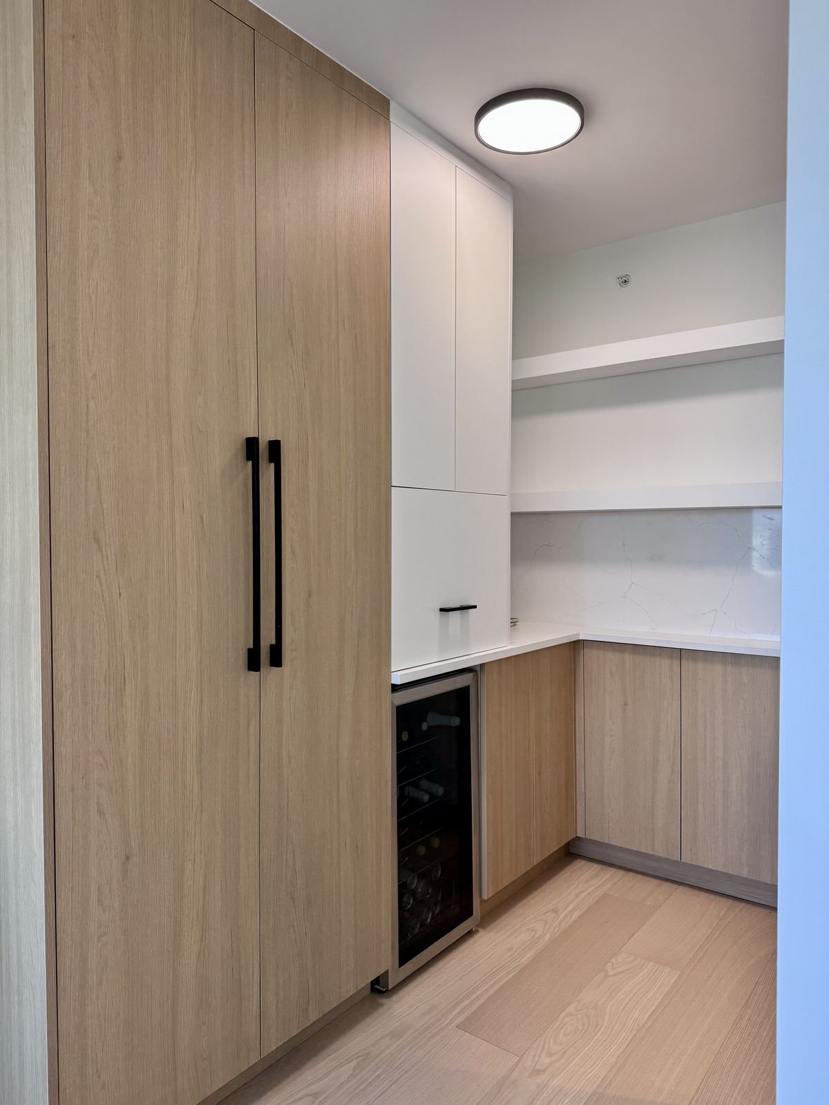 Tall pantry and L-shaped custom millwork with wood-grain and white cabinets in a Yaletown condo kitchen