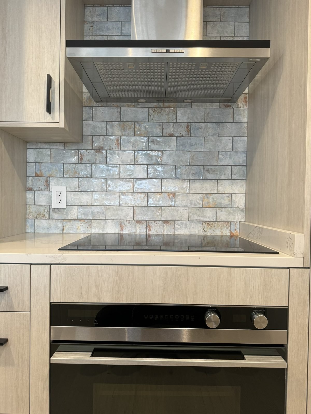 Induction cooktop, wall oven, stainless hood and textured tile backsplash in a Yaletown kitchen renovation