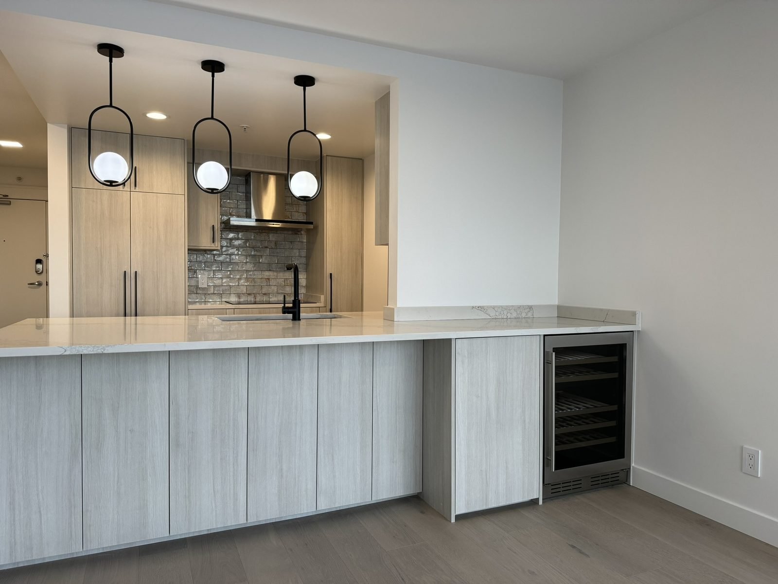 Opened-up Yaletown condo kitchen with a quartz waterfall island, wine fridge and pendant lights