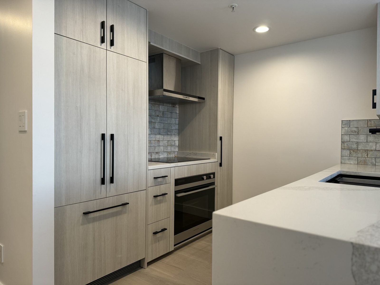 Panel-ready fridge and wall oven in tall wood-grain cabinets in a Yaletown condo kitchen renovation