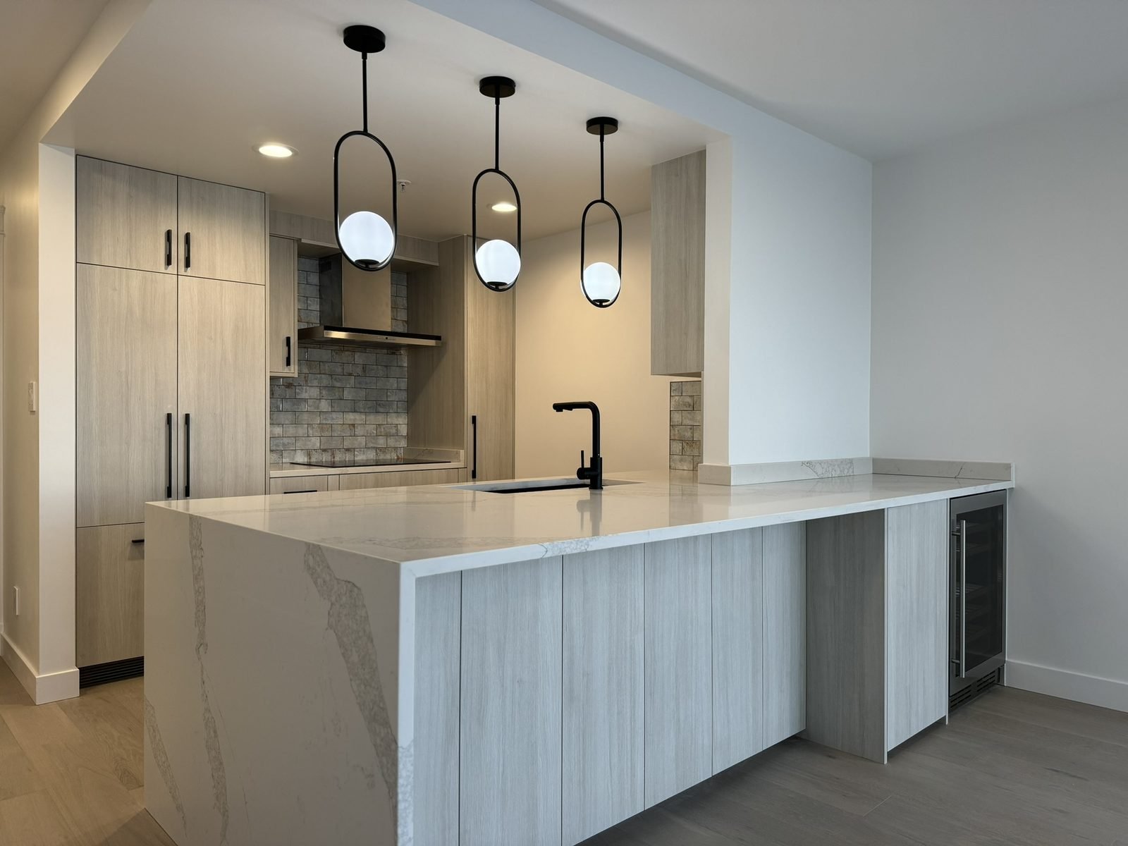 Quartz waterfall island with black undermount sink and three pendant lights in a Yaletown condo kitchen