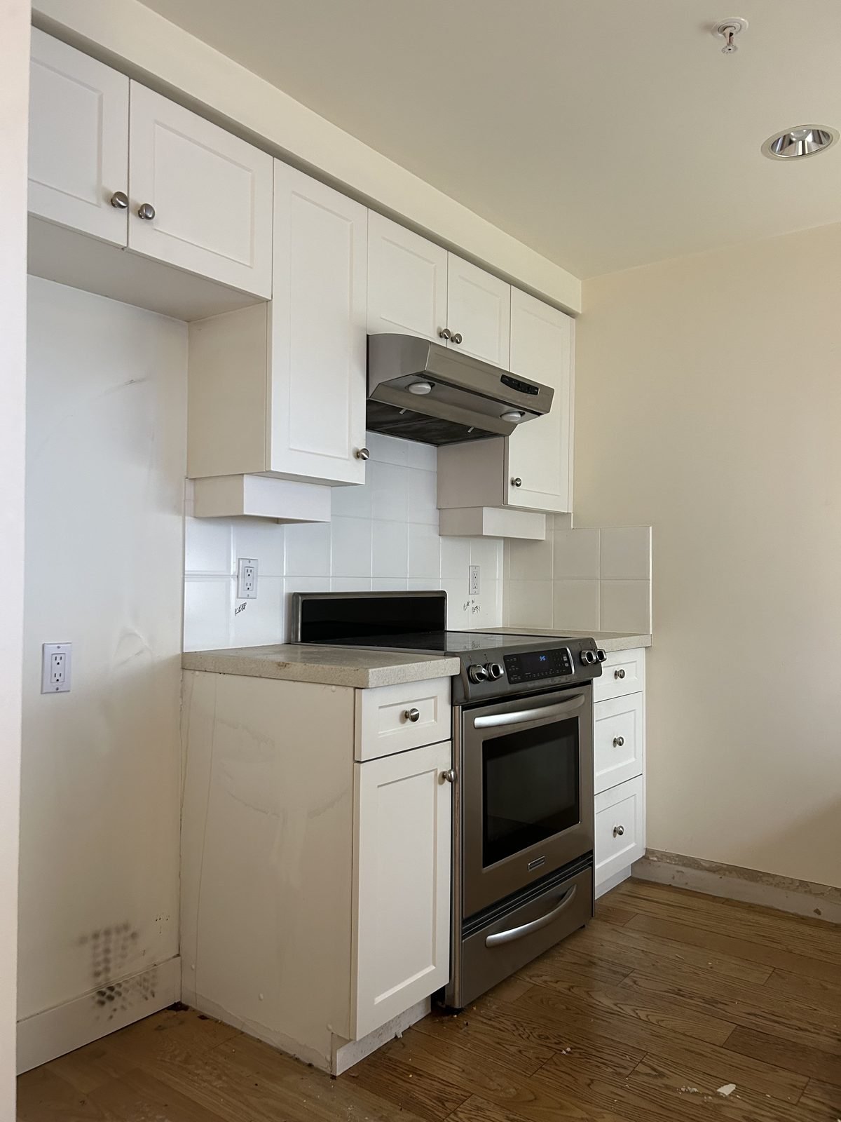 Before: enclosed range wall with white cabinets and a small hood in a Yaletown condo kitchen